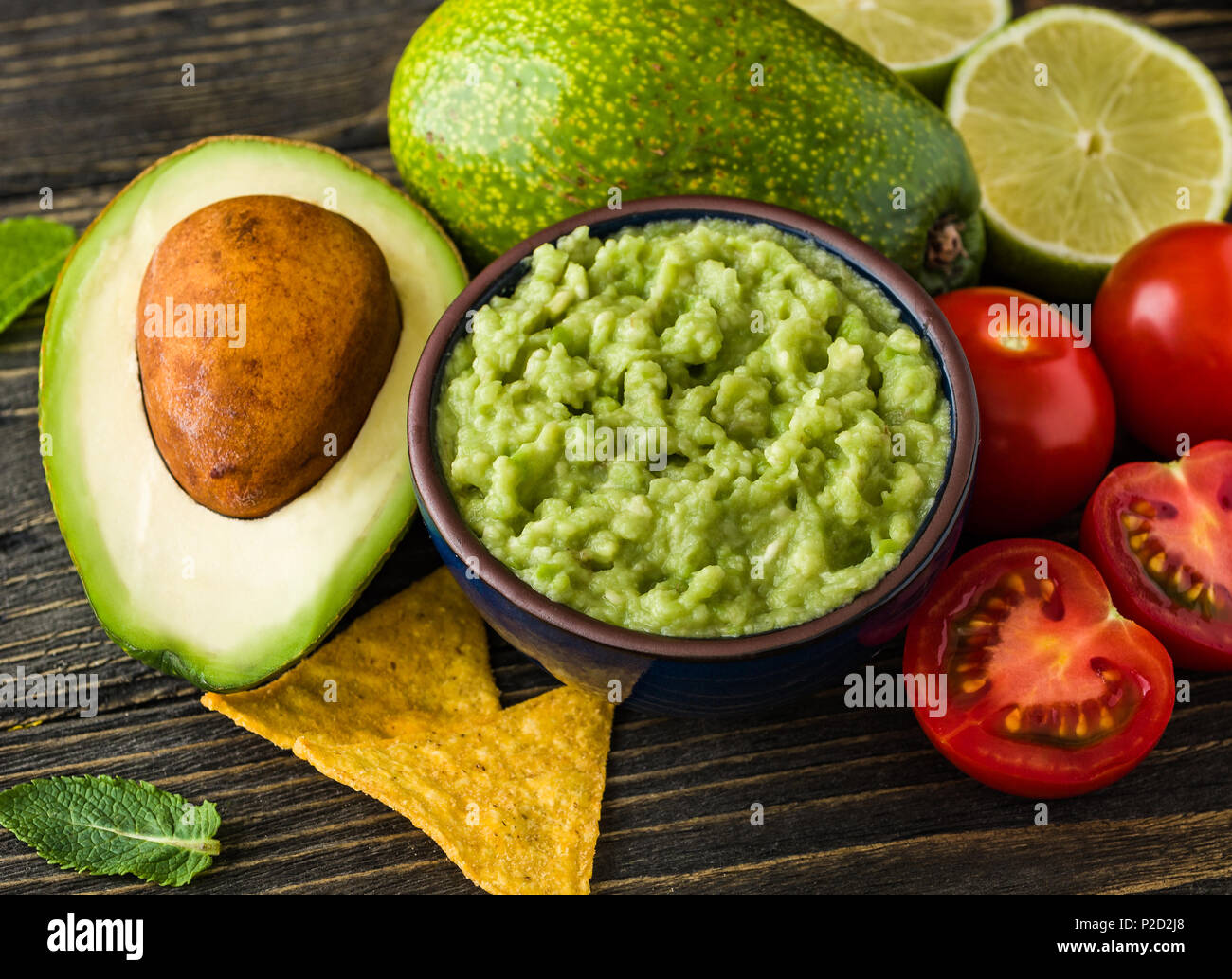 Guacamole in blauer Schüssel mit Tortilla Chips und Zitrone auf natürliche Holzschreibtisch. Stockfoto