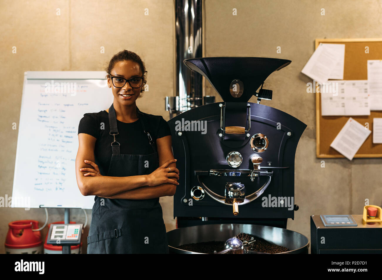 Weibliche barista stand neben Kaffee Röstung Maschine im Coffee Shop. Lächelnd Geschäft Inhaber an einer Kamera suchen. Stockfoto