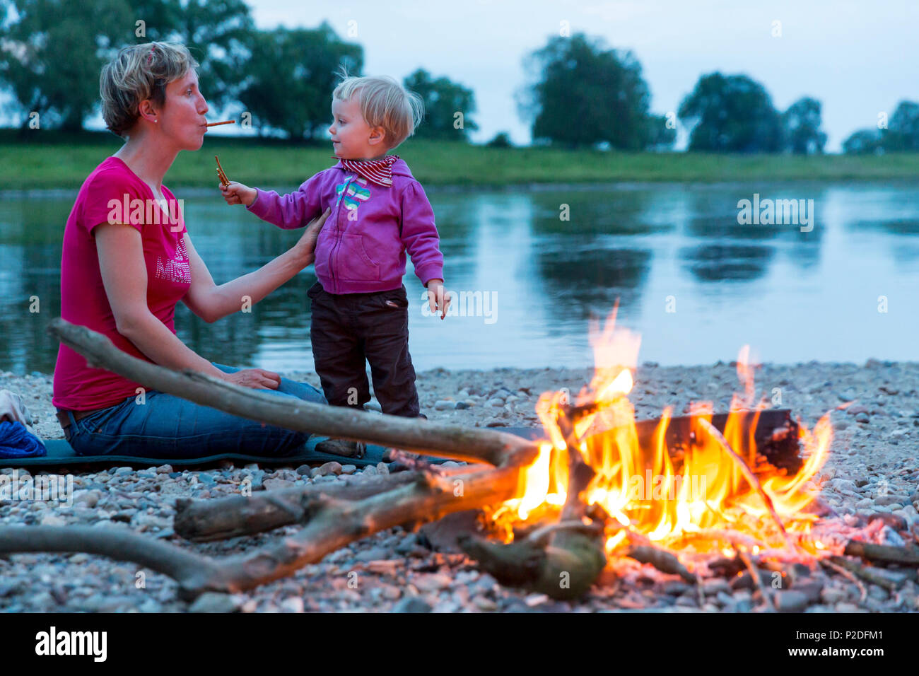 Mutter und Tochter machen Brot auf einem Stick am Lagerfeuer, Camping an der Elbe entlang, Familie Radtour entlang des Flusses E Stockfoto