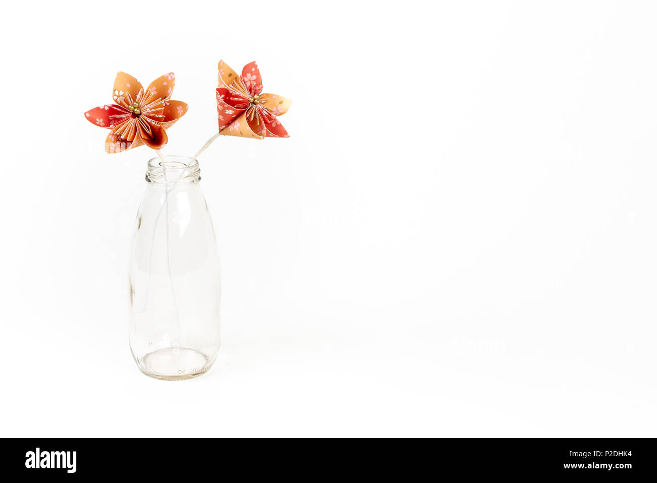Zwei orange origami Blumen in Glasfläschchen auf weißem Hintergrund. Stockfoto