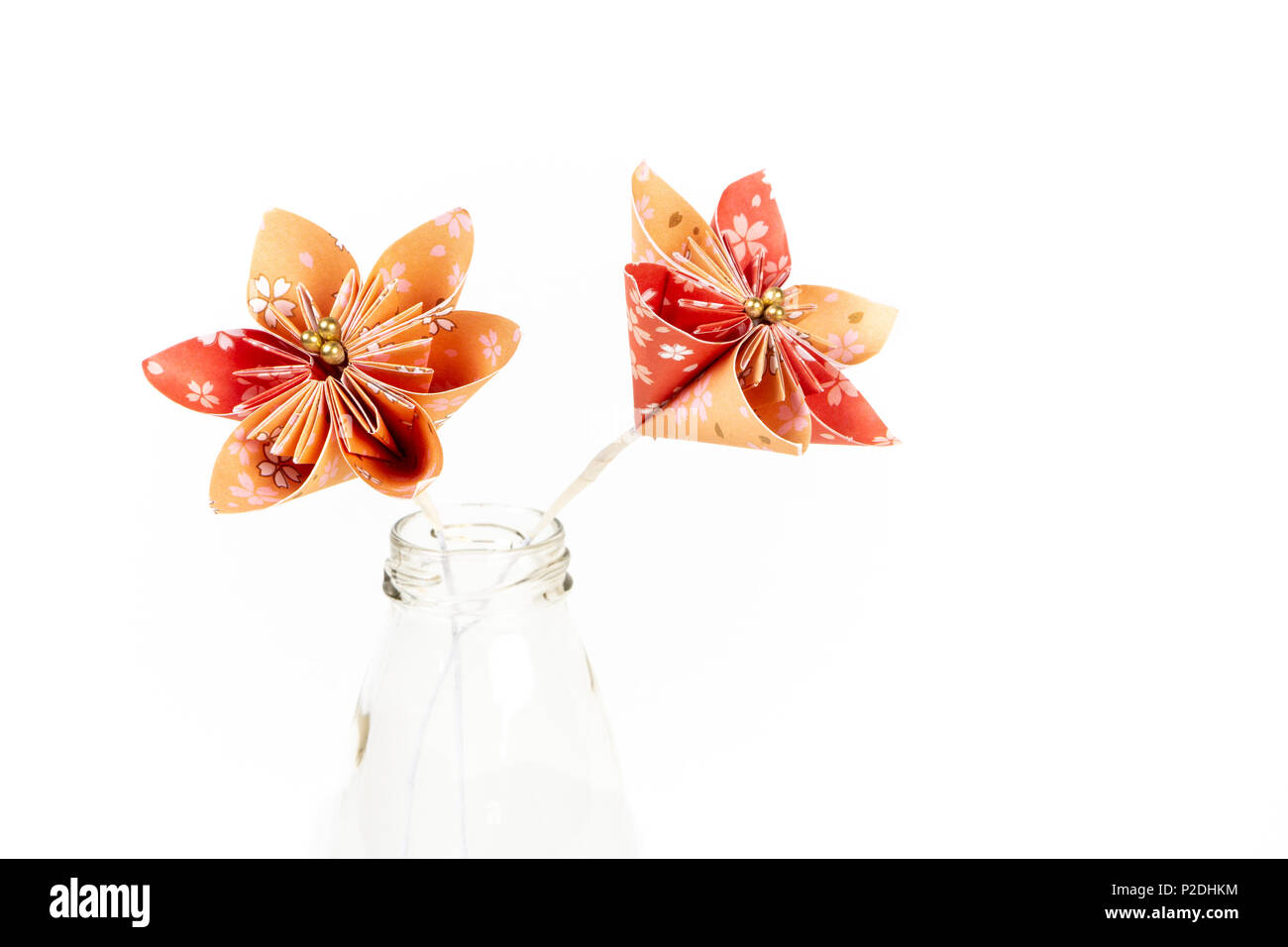 Zwei orange origami Blumen in Glasfläschchen auf weißem Hintergrund. Stockfoto