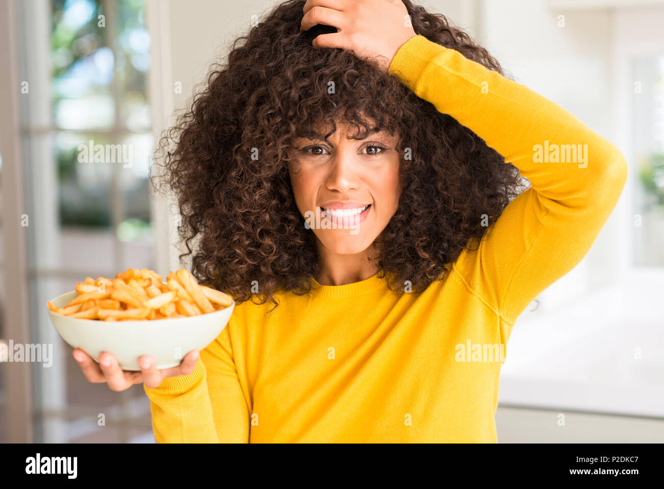 African American woman holding eine Platte mit Kartoffelchips zu Hause mit der Hand betonte am Kopf, mit Scham und Überraschung Gesicht schockiert, wütend und frustriert Stockfoto