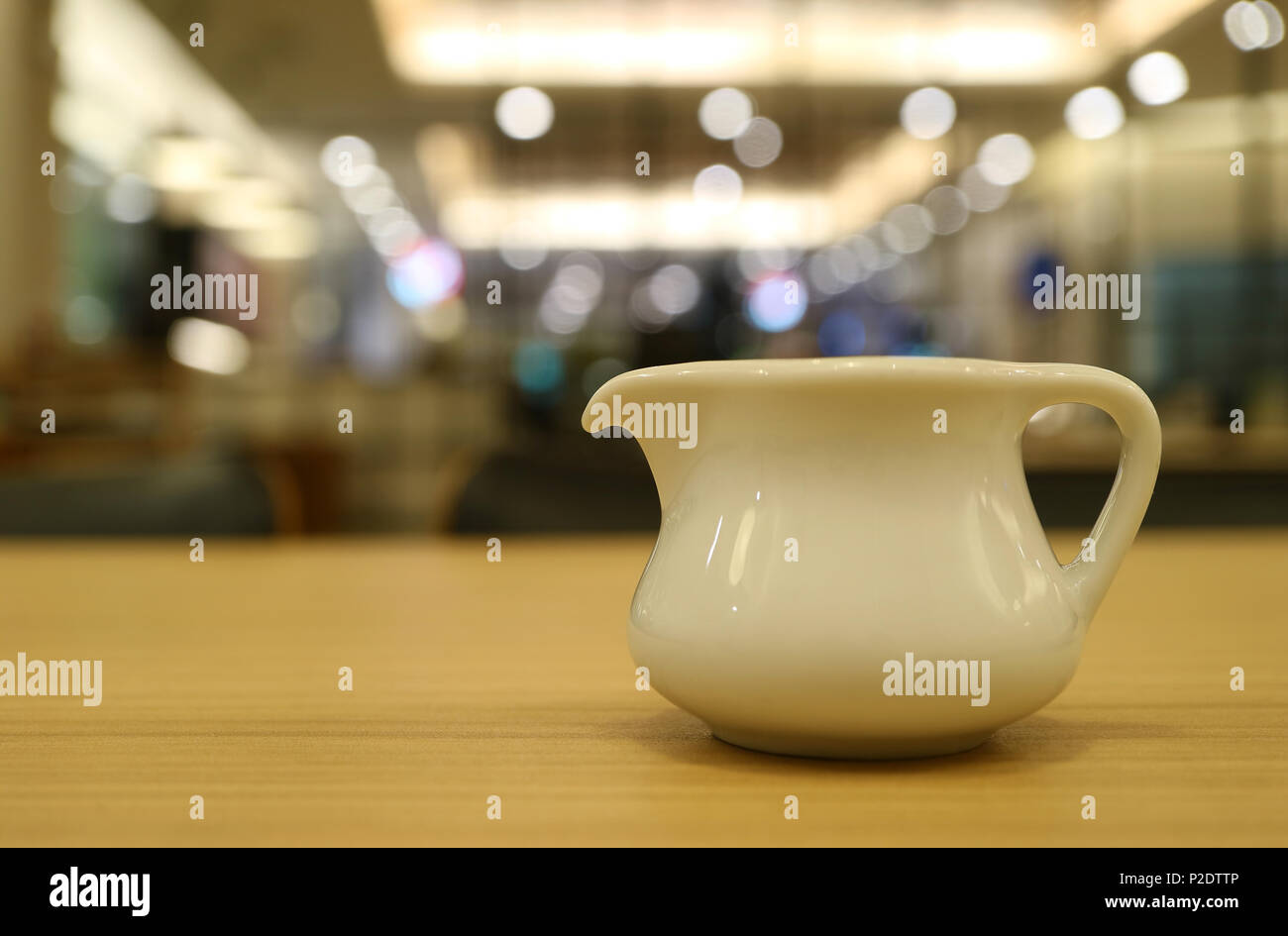 Geschlossen bis ein weißer Keramik Krug auf Holz- Cafe's Tabelle mit bokeh Innenbeleuchtung im Hintergrund Stockfoto