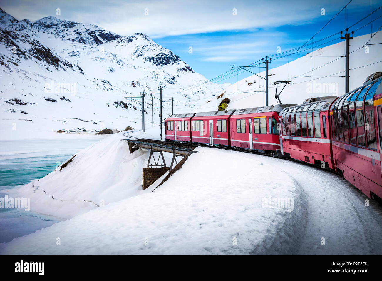 Bernina Express Zug, einer der höchsten Bahn der Welt, geht über eine kleine Brücke im verschneiten Berg in der Nähe eines zugefrorenen See Stockfoto
