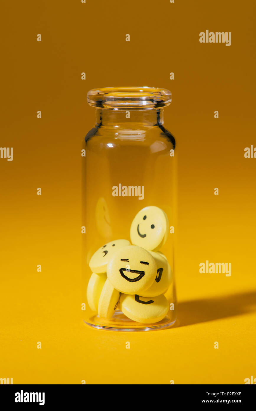Nahaufnahme von Pillen mit smiley-Gesichter in Glasflasche auf Gelb Stockfoto