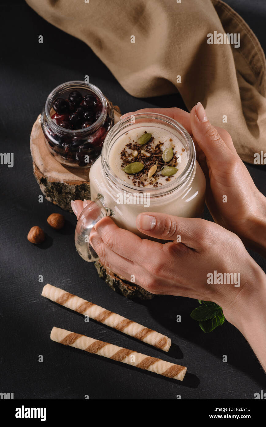 Zugeschnittenes Bild der weiblichen Holding Milchshake mit Schokolade rasieren und Pistazien, süße Strohhalme, Korinthen, Walnüsse und Minze Stockfoto