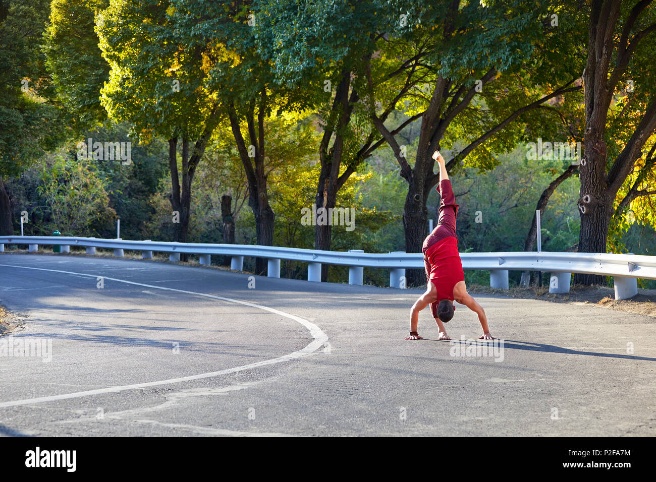 Passen Mann im roten Kostüm Yoga auf der Asphaltstraße in Almaty, Kasachstan Stockfoto