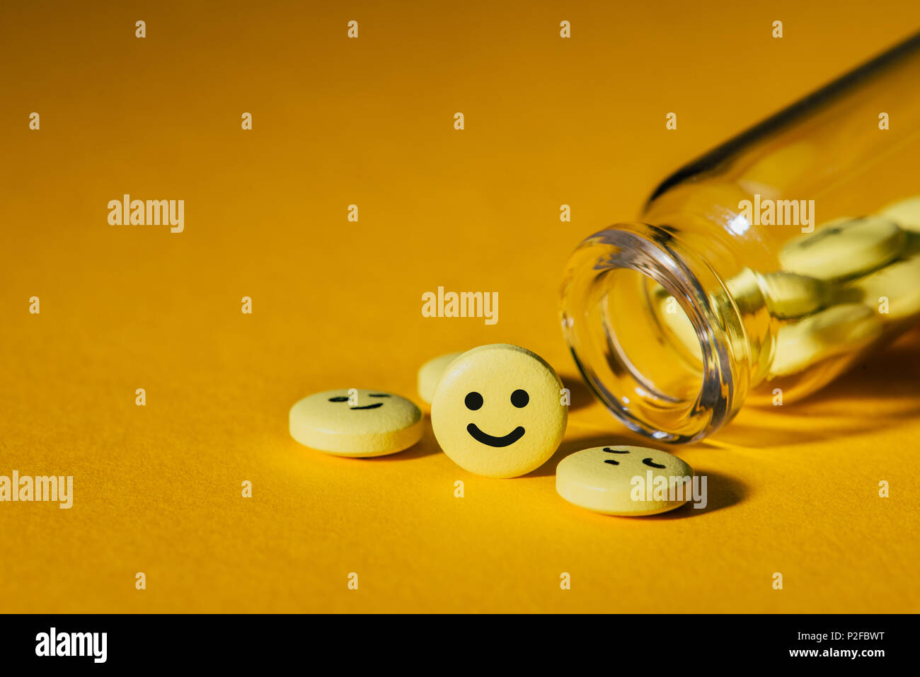 Nahaufnahme von Pillen mit Smileys und Glas Flasche auf Gelb Stockfoto