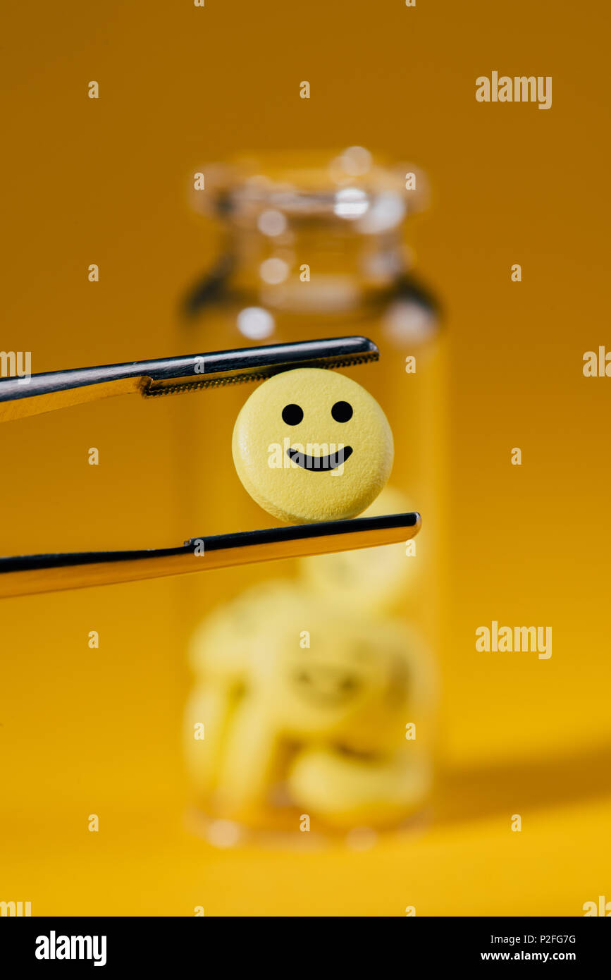 Nahaufnahme der Pille mit Smiley in Pinzette und Glas Flasche auf Gelb Stockfoto