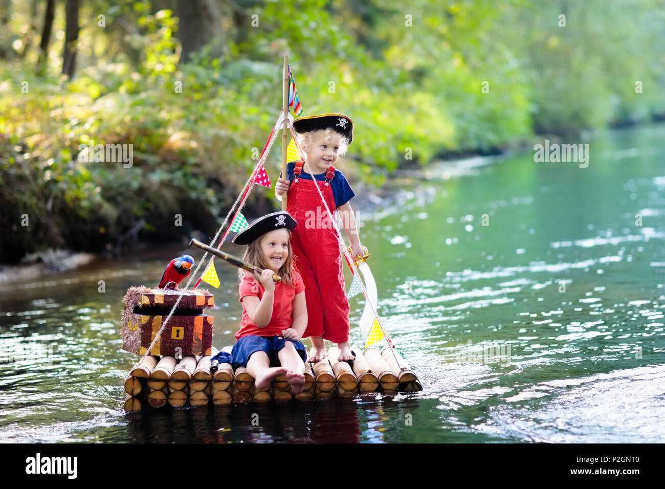 Kinder gekleidet in Piraten Kostüme und Hüte mit Schatztruhe, Ferngläser und Schwerter spielen auf hölzerne Floß Segeln in einem Fluss an heißen Sommertag. Pira Stockfoto