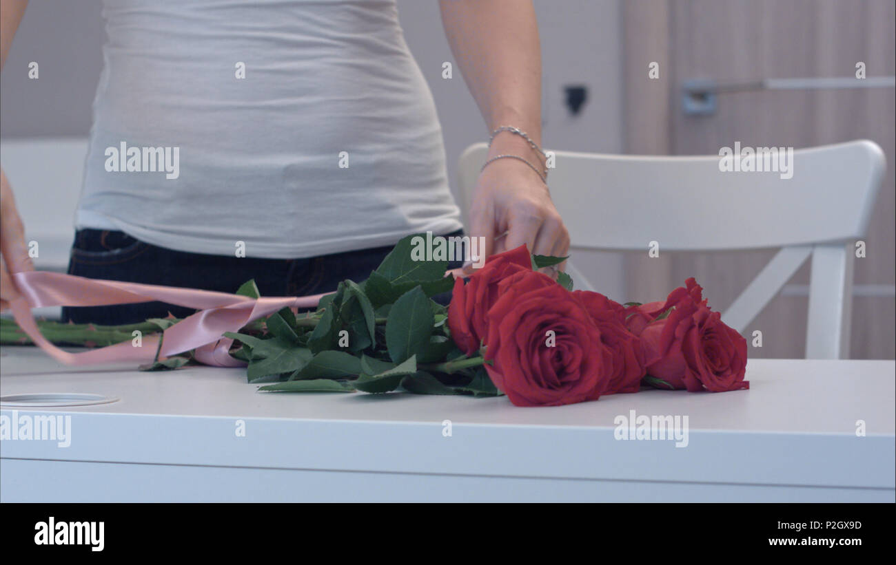 Junge Frau binden einer Schleife auf rote Rose Bouquet Stockfoto