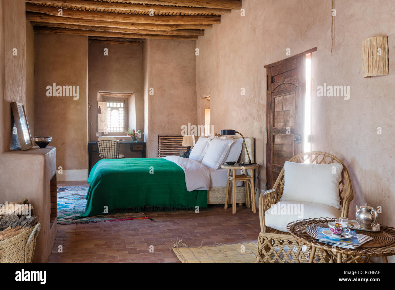 Rattan Sessel und Tisch im Vordergrund der Schlafzimmer mit Holzdecke, Erde Wänden und Terrakottafußboden. Stockfoto