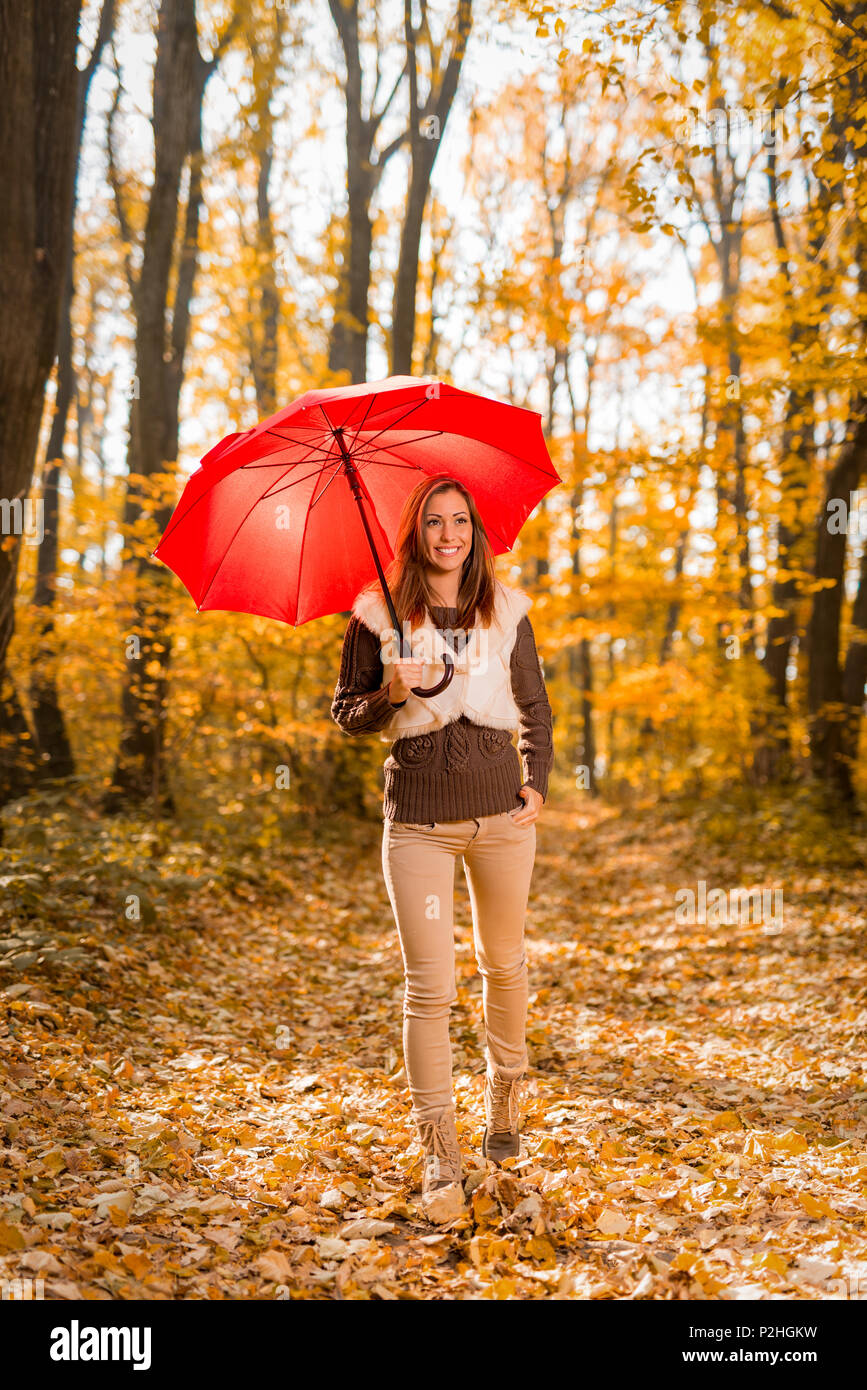 Schöne junge Frau mit roten Regenschirm durch die sonnigen Wald im Herbst Farben. Stockfoto