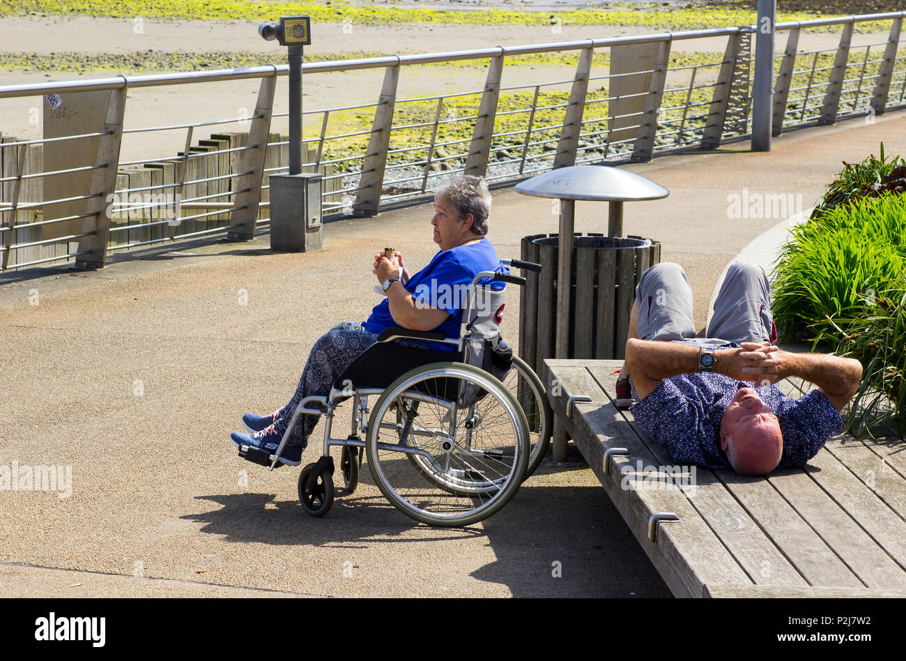 Vom 7. Juni 2018 Eine ältere behinderte Dame mit ihrem Partner in der Sonne an der Promenade von Newcastle County Down in Nordirland entspannen Stockfoto