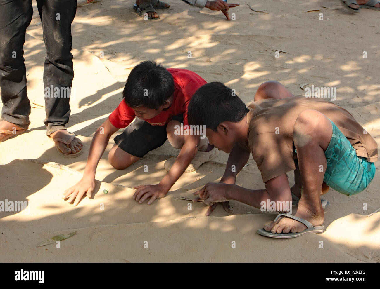 Zwei kambodschanische Jungs, das Spiel von Marmor, mit kleinen Kugeln aus Glas, auf die raue Sandboden des Pakets mit der Verpackungsnaht Schule Spielplatz. Stockfoto