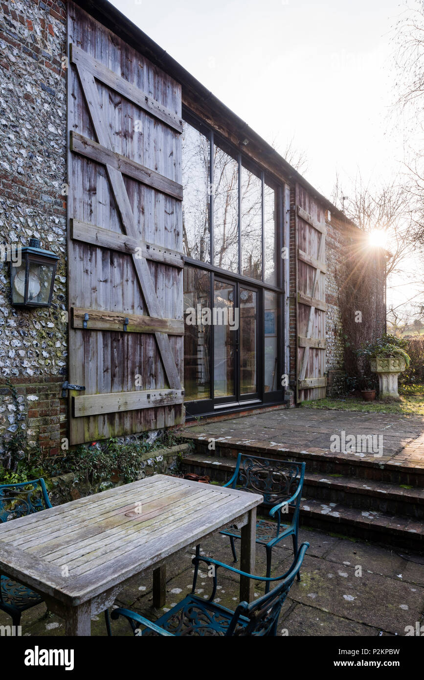 Gartenmöbel auf der Terrasse der Scheune mit großen Fenstern und Fensterläden aus Holz, Sussex Stockfoto