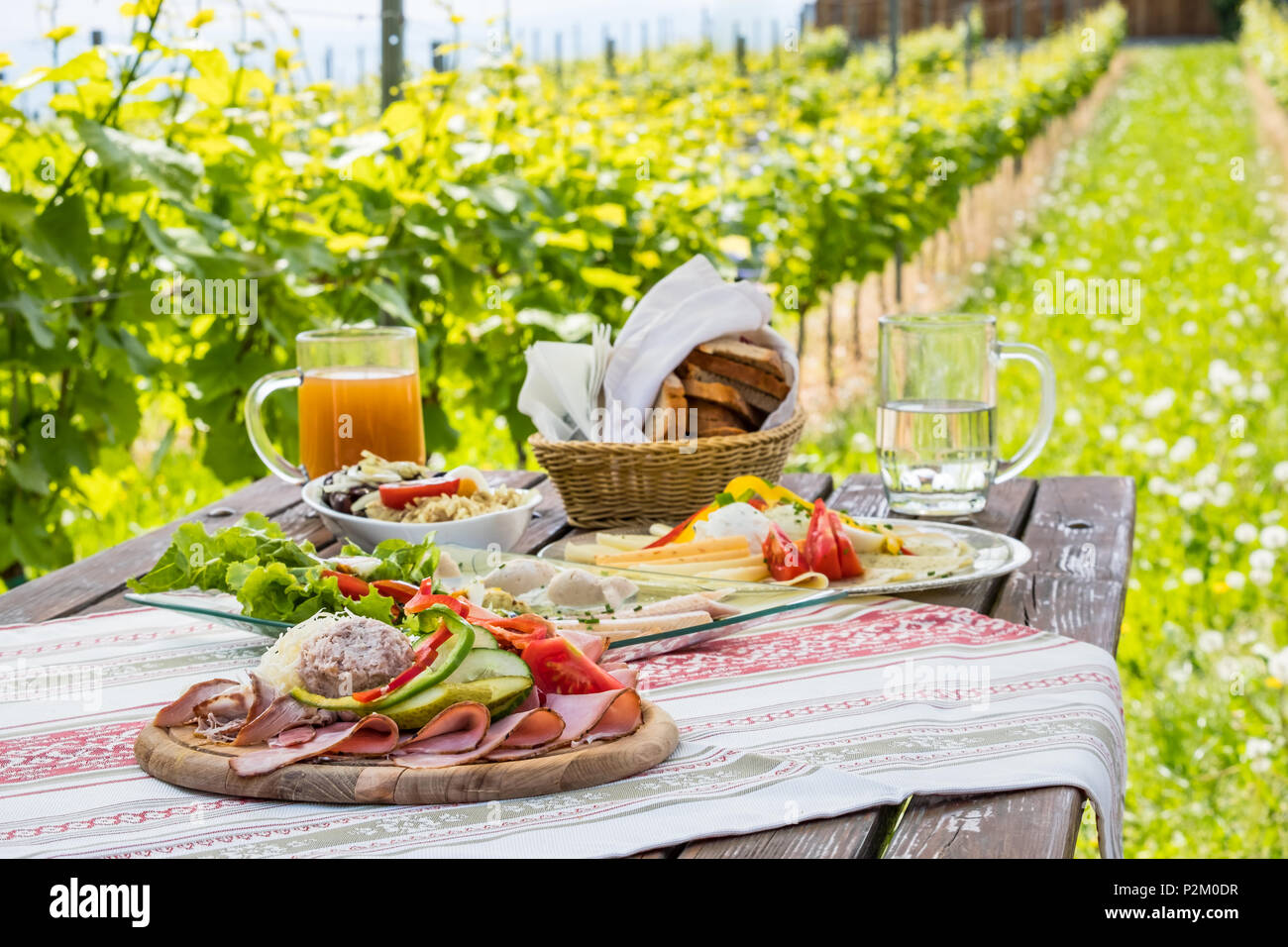Brettljause, traditionelle kalte Platte mit Fleisch, Käse, Fisch, Gemüse, Brot und Getränke auf Holztisch im Weinberg mit Hütte in der Steiermark, Österreich Stockfoto