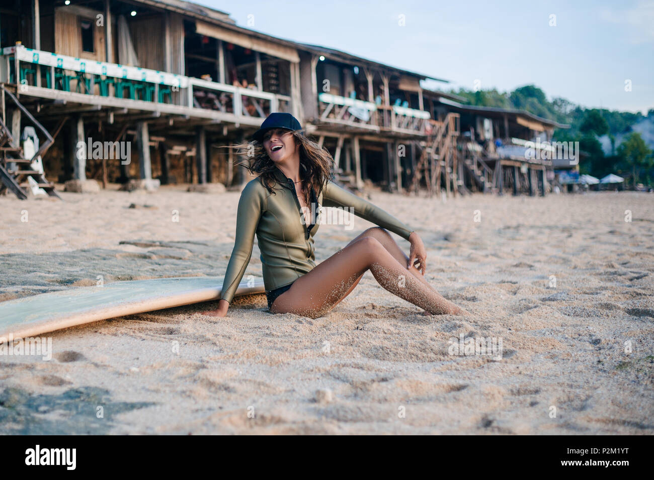 Junge Frau in Neoprenanzug sitzen auf Surfboard am Strand Stockfoto