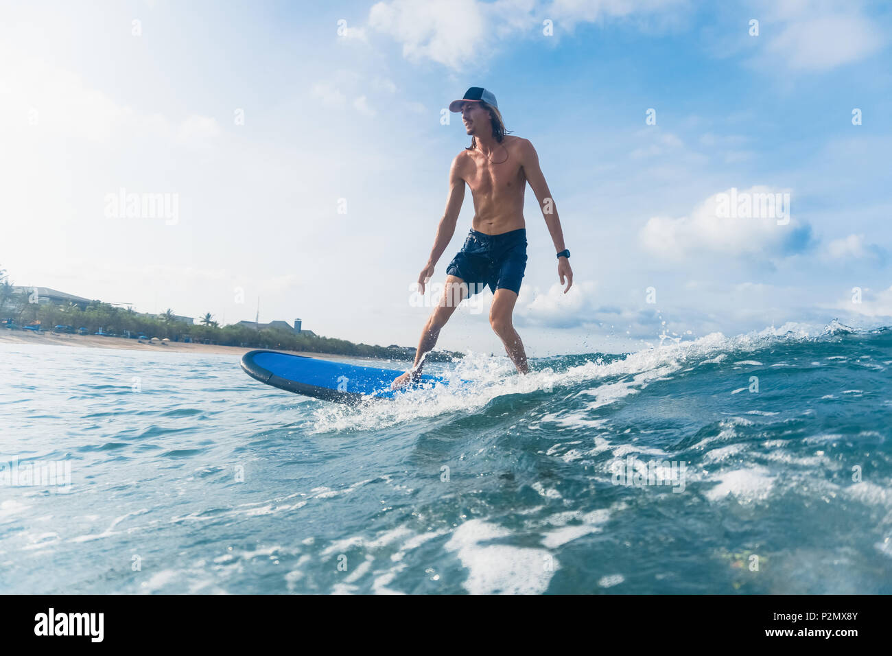 Seitenansicht des Menschen in Badeshorts und Kappe Surfen im Ozean Stockfoto