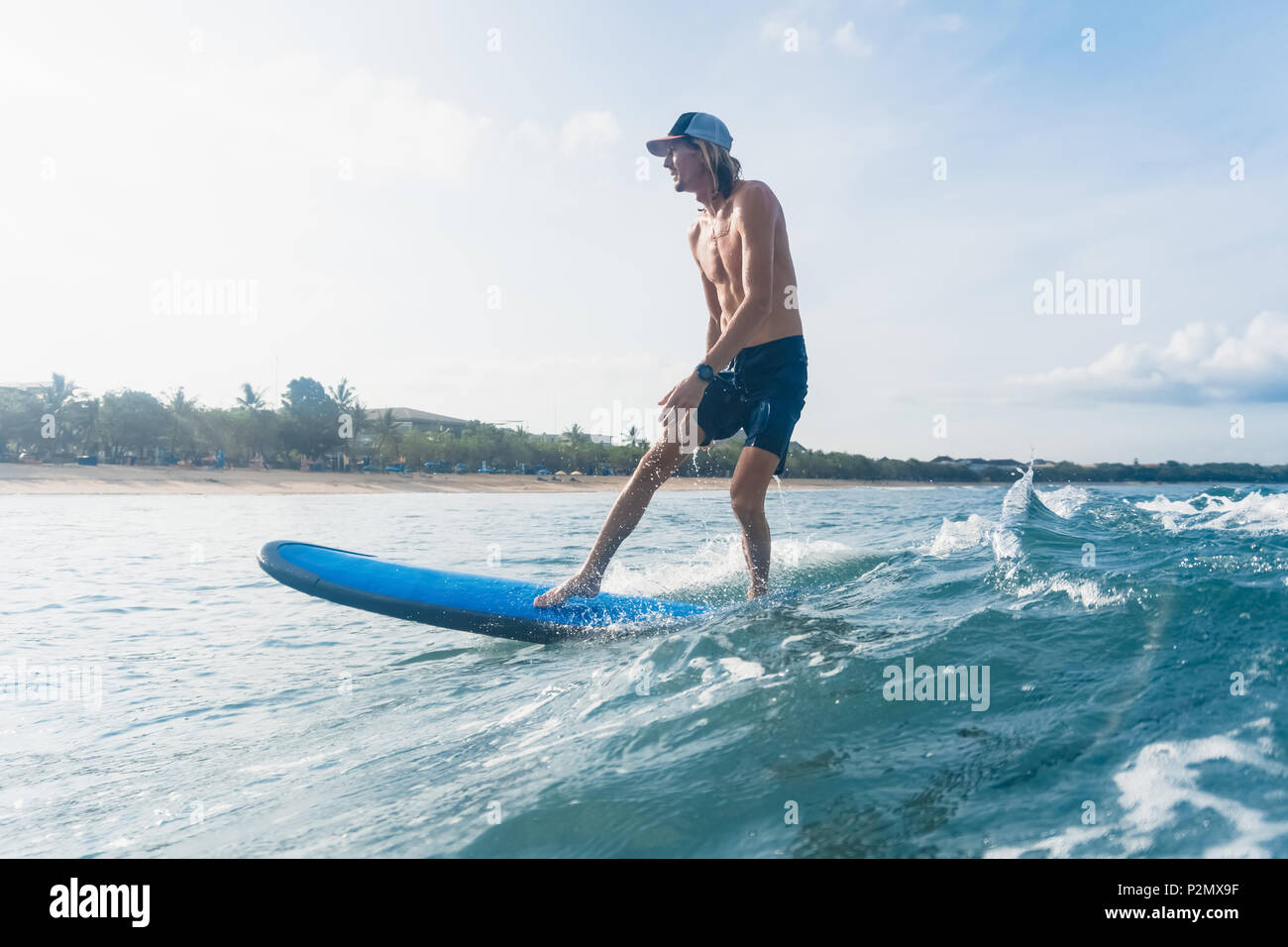 Seitenansicht des Menschen in Badeshorts und Kappe Surfen im Ozean Stockfoto