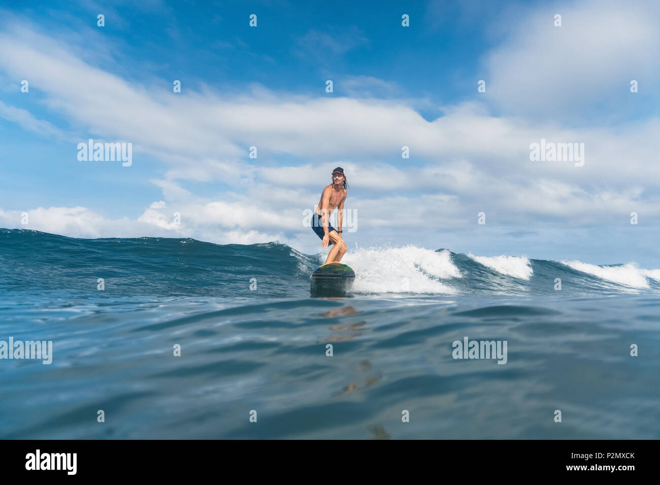 Schöner Mann in Badeshorts und Kappe Surfen im Ozean Stockfoto