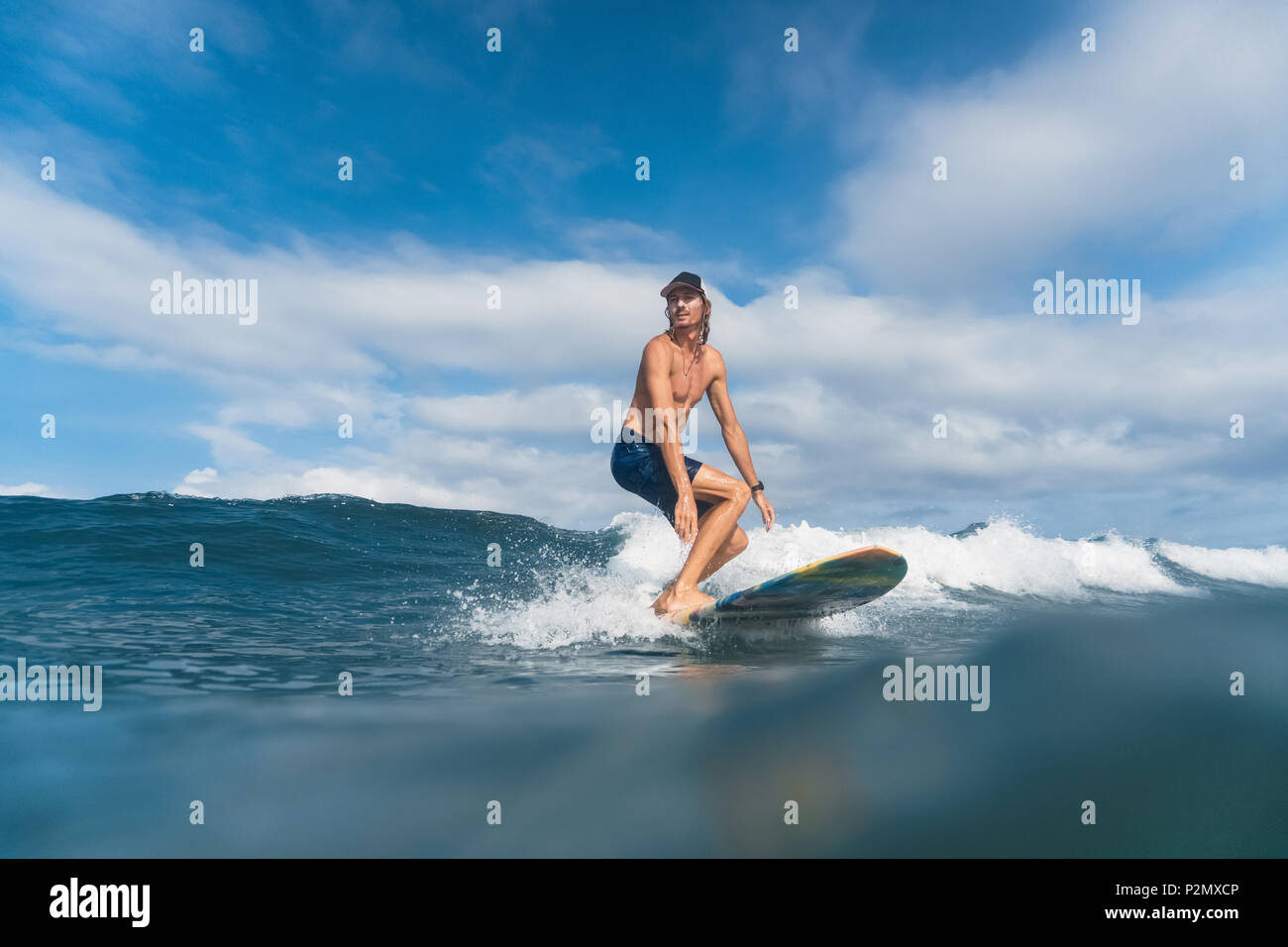 Schöner Mann in Badeshorts und Kappe Surfen im Ozean Stockfoto