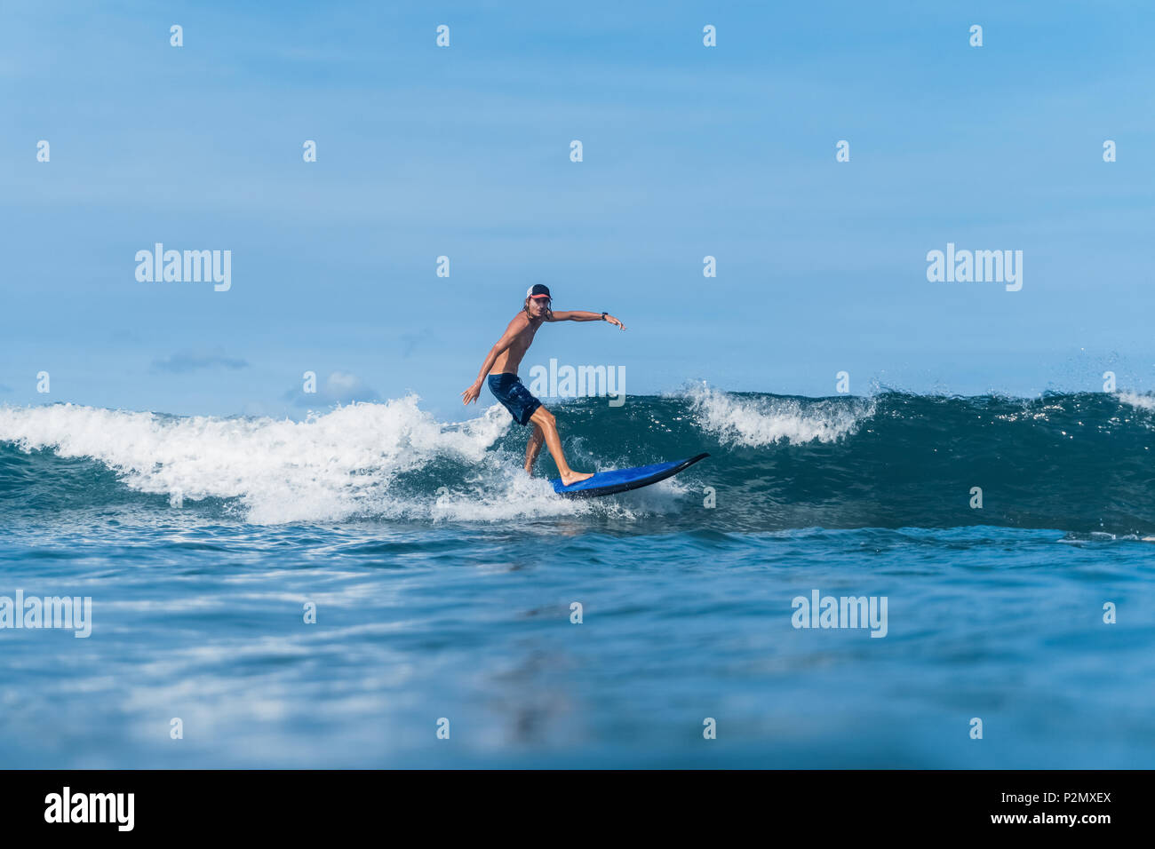 Mann in Badeshorts und Kappe Surfen im Ozean Stockfoto
