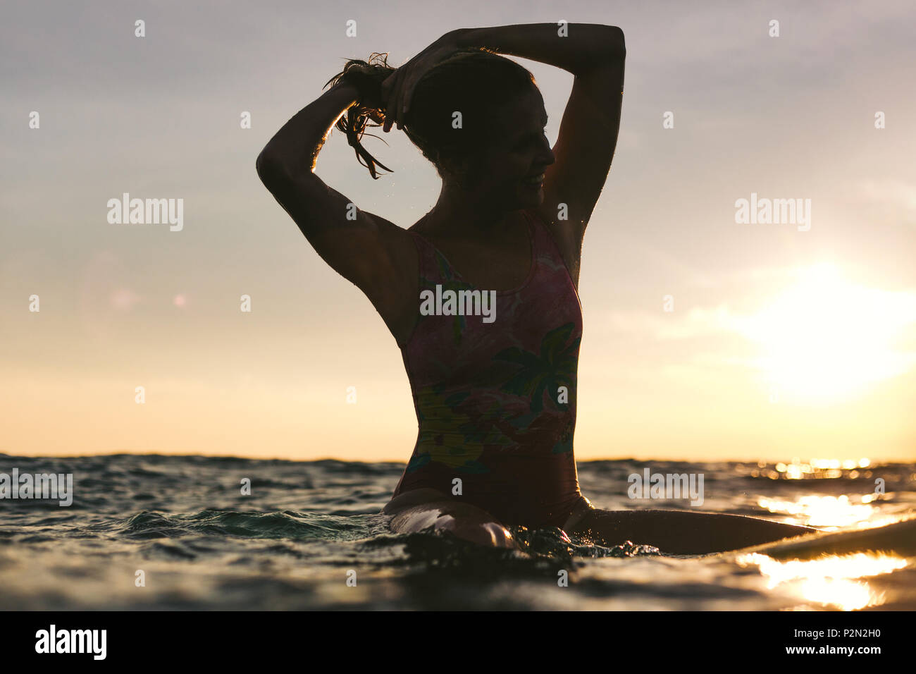 Silhouette einer Frau nachstellen Haar beim Sitzen auf Surfen im Ozean auf Sonnenuntergang Stockfoto