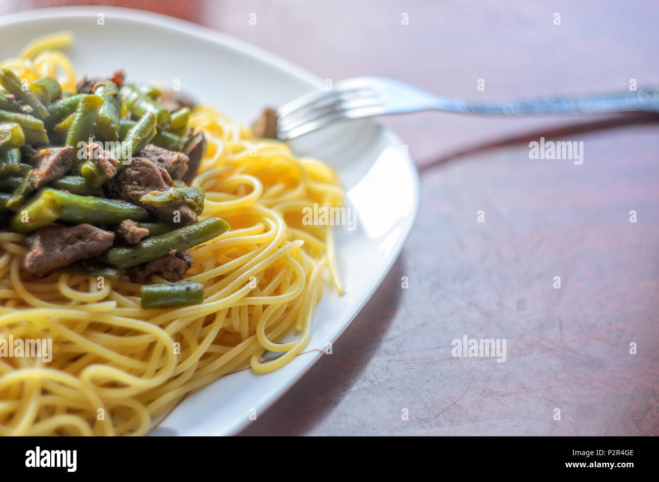 Große weiße Platte mit heißem Leckere Pasta mit Fleisch und grüne Bohnen auf einer glänzenden Tisch. Spaghetti Gericht Hintergrund Stockfoto
