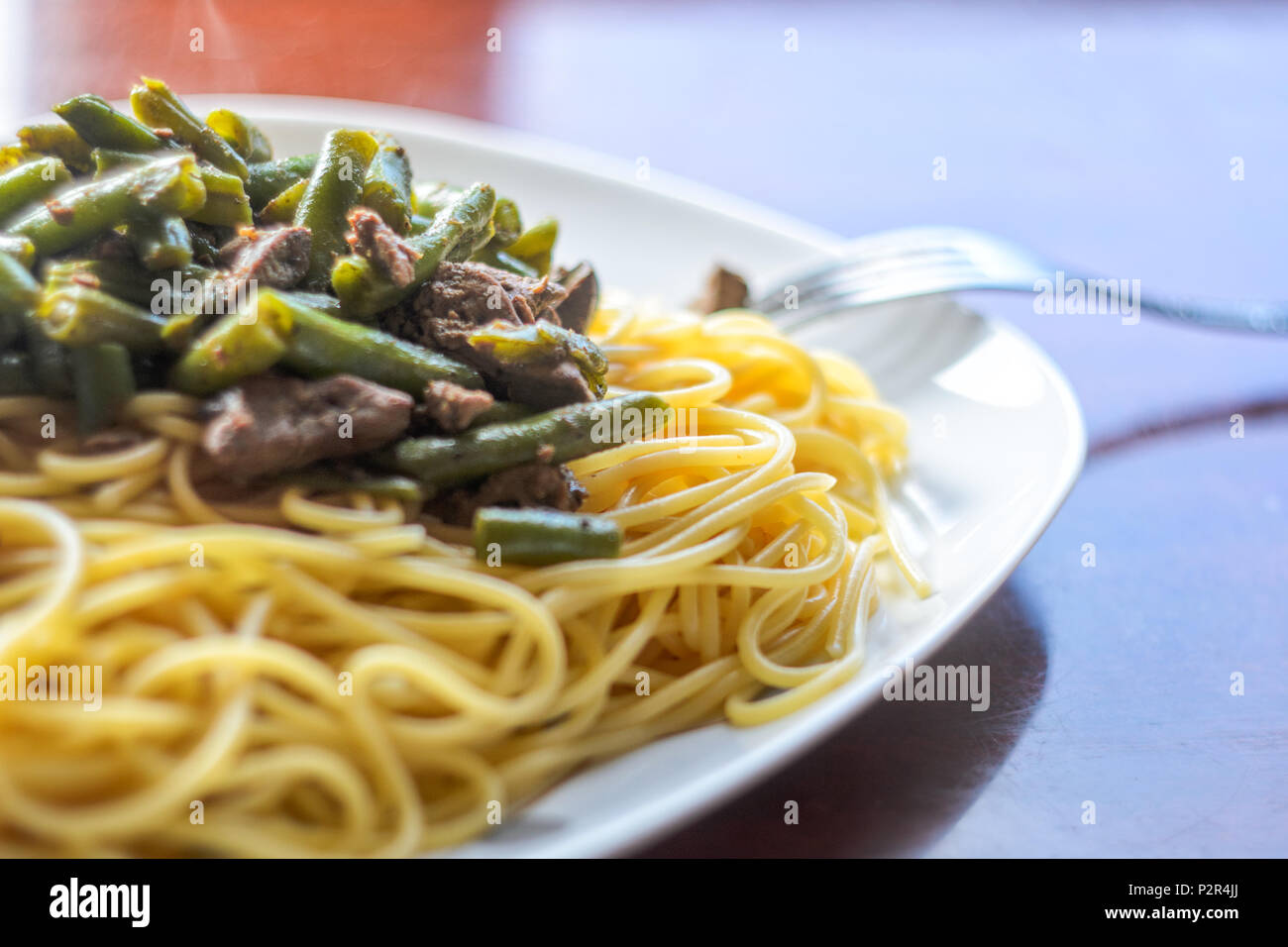 Große weiße Platte mit heißem Leckere Pasta mit Fleisch und grüne Bohnen auf einer glänzenden Tisch. Spaghetti Gericht Hintergrund Stockfoto