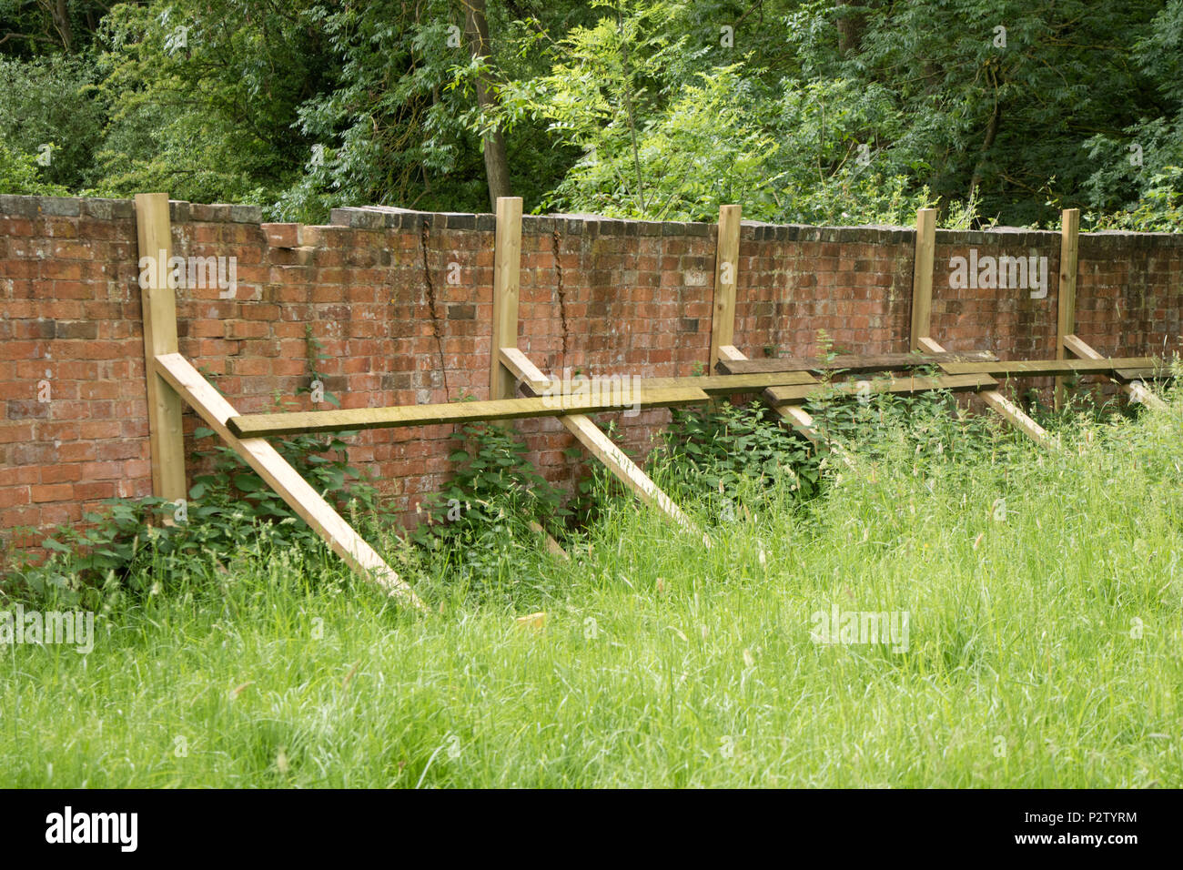 Eine Gartenmauer in der Gefahr des Zusammenbruchs, mit Holzbohlen, England zu unterstellenden, Großbritannien Stockfoto