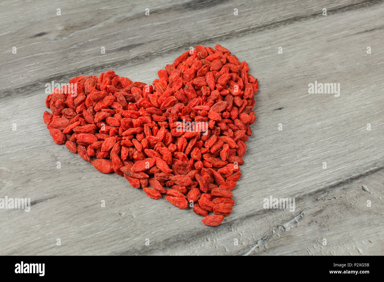 Haufen Goji Beeren (wolfsbeere - Lycium chinense) getrocknete Früchte in Form von Herzen auf einem grauen Holz Tisch angeordnet. Stockfoto