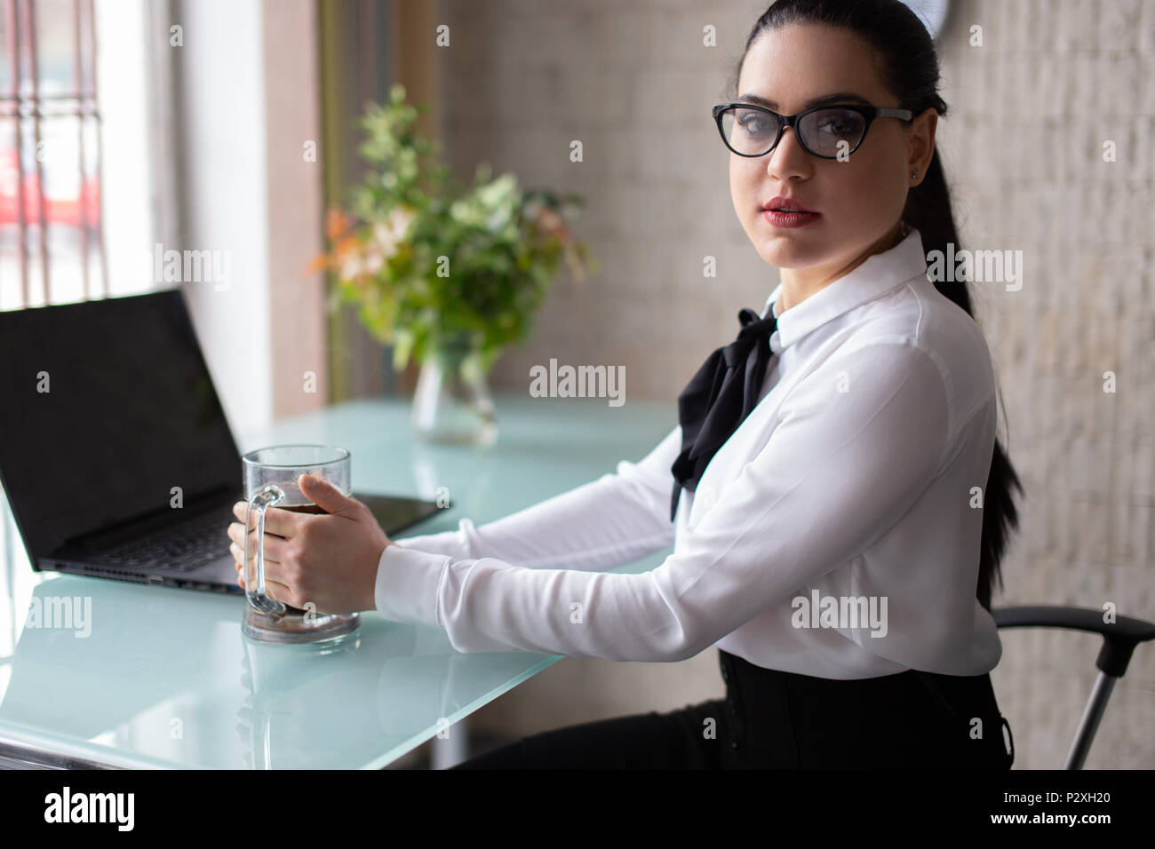 Junge intelligente Geschäftsfrau mit großen Becher Kaffee im Büro Stockfoto