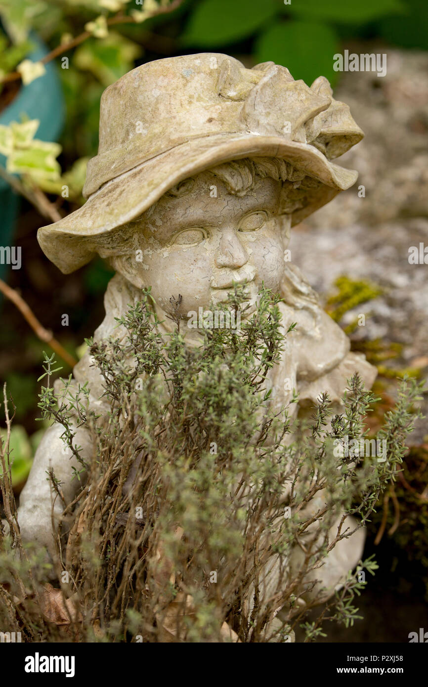 Eine steinerne Figur eines Jungen in der Nähe eines Gartenteiches neben einem Topf Thymian. Lancashire North West England UK GB Stockfoto