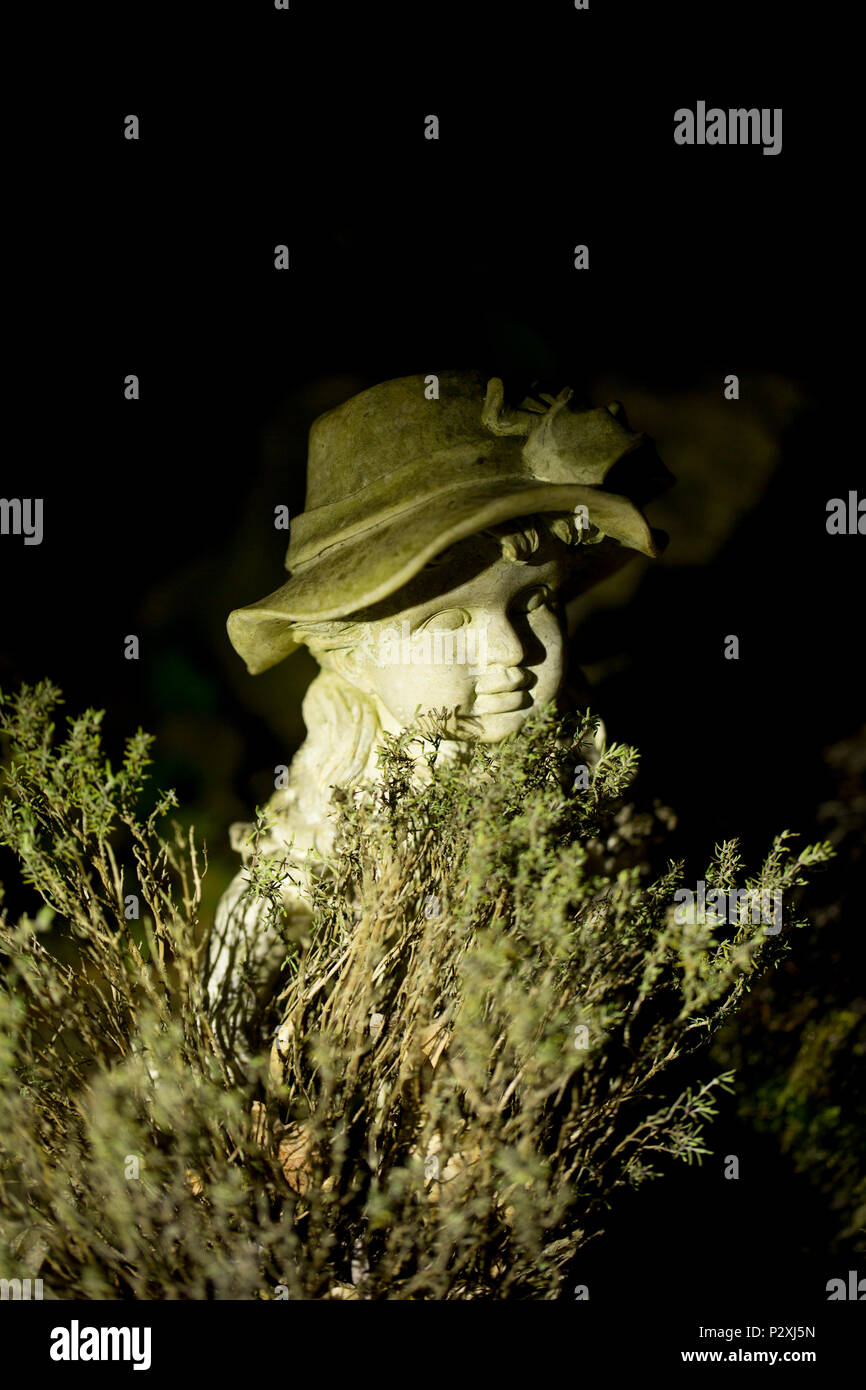Eine steinerne Figur eines Jungen in der Nähe eines Gartenteiches neben einem Topf Thymian, bei Nacht fotografiert. Lancashire North West England UK GB Stockfoto