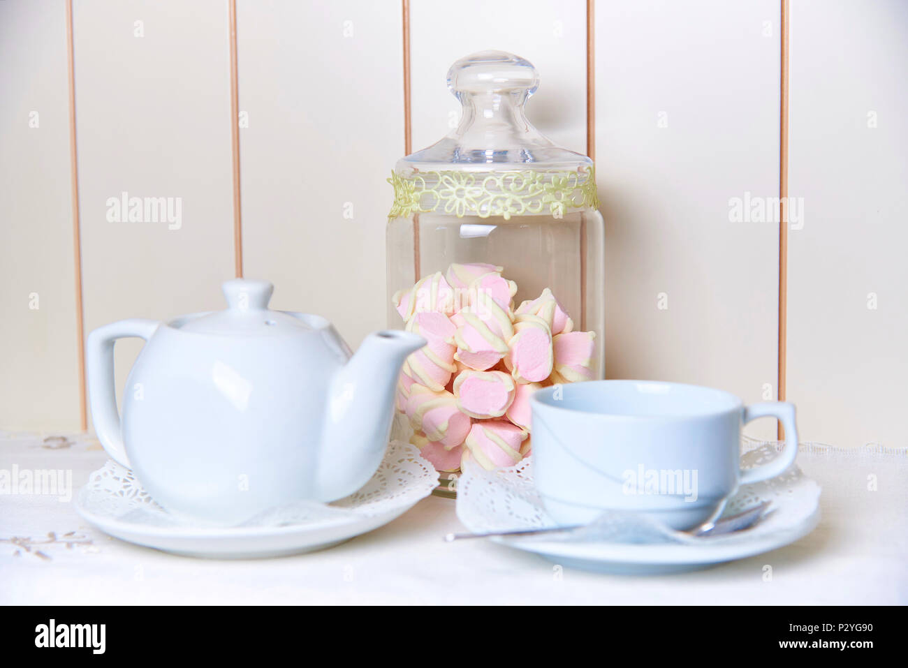 Ein Glas Glas Marshmallow steht hinter einen Wasserkocher und eine Schale auf eine Untertasse mit Spitze. Stockfoto