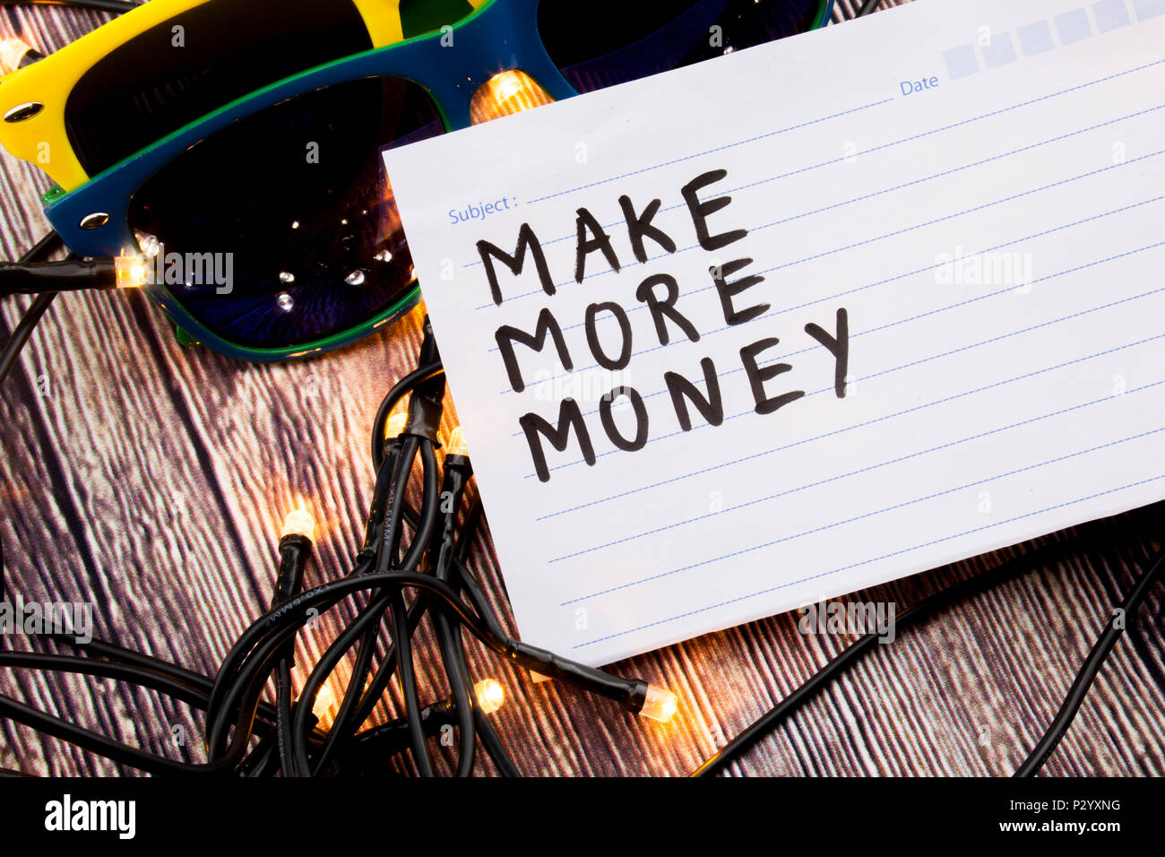 Mehr Geld, handgeschrieben auf Register Seite mit schwarzer Farbe. Zwei Sonnenbrillen in verschiedenen Kombinationen von Farben, die Licht in einer zufälligen Reihenfolge Stockfoto