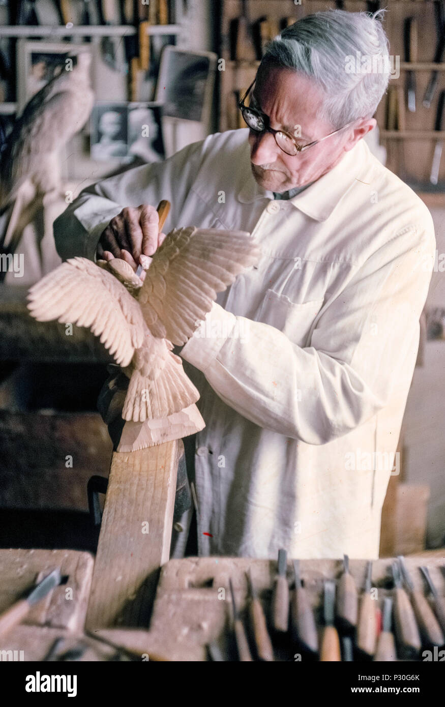 Ein Schweizer Holzschnitzer verwendet eine Holzschnitzerei Werkzeug und  feste Hand ein Vogel mit ausgebreiteten Flügeln aus einem Block von Holz in  seinem Laden im Dorf am Seeufer von Brienz, Schweiz zu erstellen.