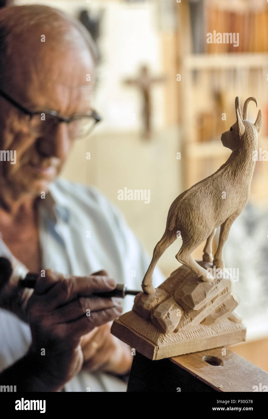Ein Schweizer Holzschnitzer verwendet eine Holzschnitzerei Werkzeug und  verlässliche Hände einer Bergziege aus einem Block von Holz in seinem Laden  im Dorf am Seeufer von Brienz, Schweiz zu erstellen. Lange das Zentrum