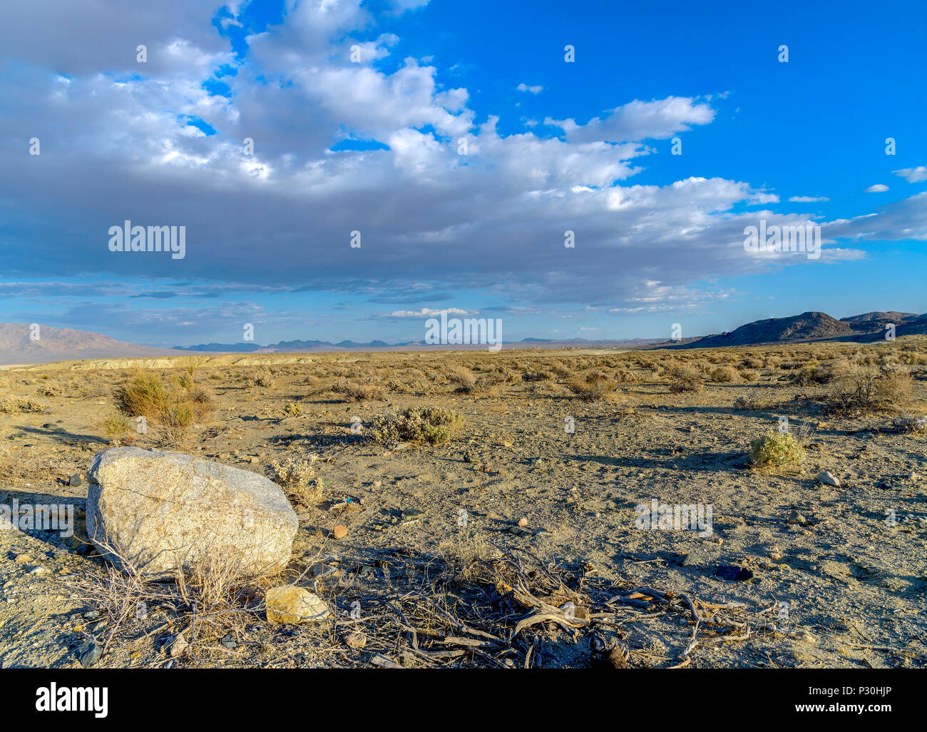 Großen Felsen im Vordergrund der Wüste mit Pinsel und Berge im Hintergrund unter einem blauen Himmel mit Wolken. Stockfoto