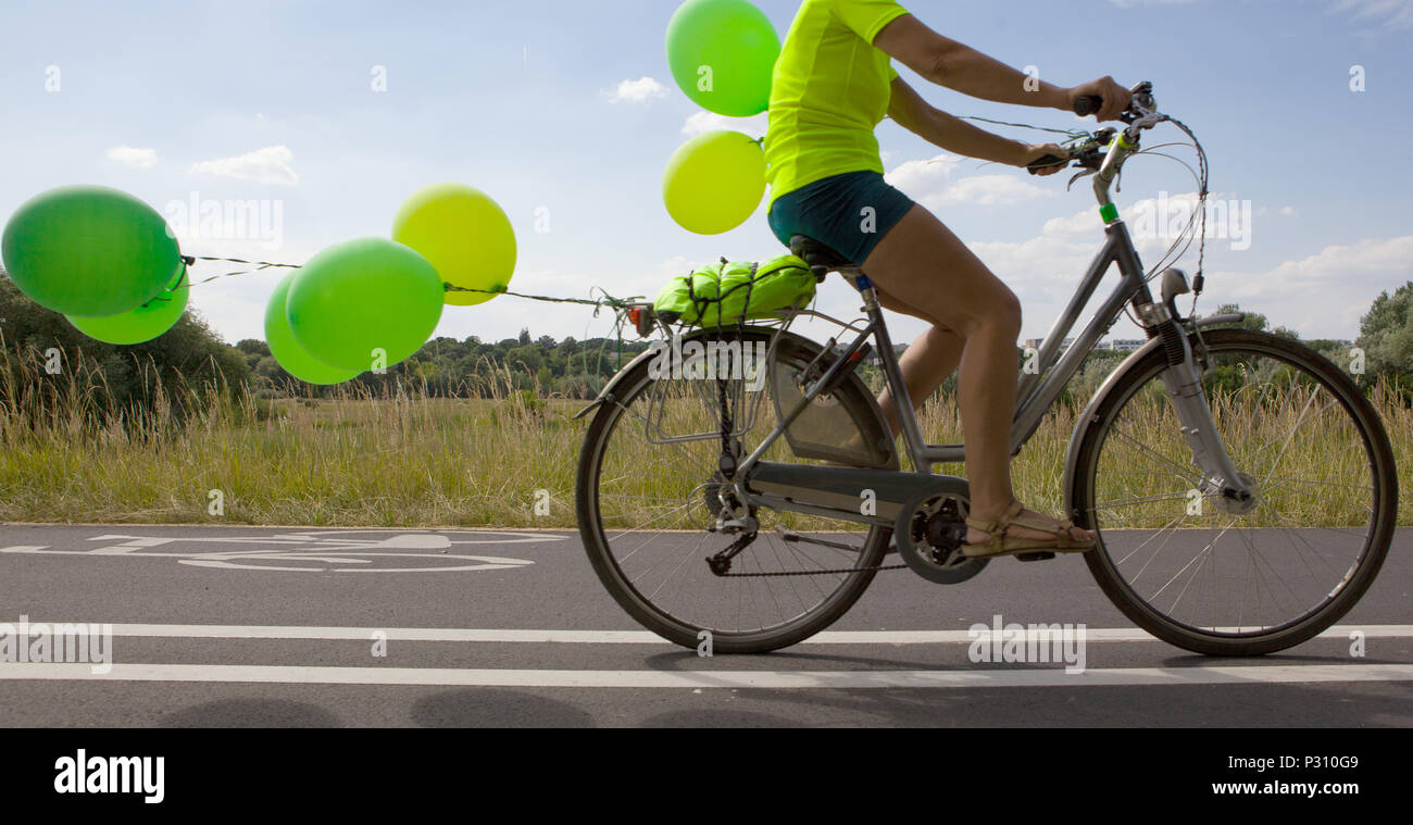 Frau auf einem Fahrrad mit Luftballons. Grüne Ballons am Fahrrad befestigt. Stockfoto