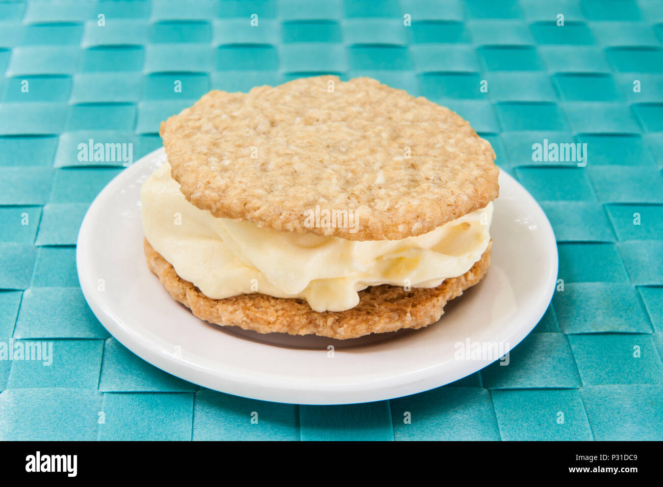 Vanille Eis zwischen zwei oatmeal Cookies auf eine weiße Platte mit einem blauen Hintergrund sandwiched Stockfoto