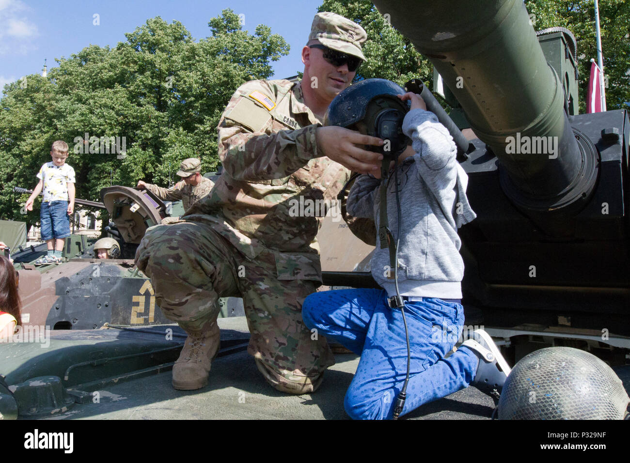 US Armee Sgt. Jeremy Carda, gebürtig aus Ogilvie, Minn, und Infanterist zugewiesen 3. kombiniert Arme Bataillon, 69. Armor Regiment, 1st Armored Brigade Combat Team, 3. Infanterie-Division, hilft eine lettische Kind Panzerhelm an eine statische Anzeige zum 25. Jahrestag der lettischen Nationalgarde in Riga, Lettland 20. August 2016 anprobieren.  Die Soldaten der 3. Mrd., 69. bestückt Rgmt., an der Veranstaltung beteiligt sind Training mit ihren baltischen Verbündeten zur Unterstützung der Operation Atlantic zu lösen, führte ein US bemüht in Osteuropa durchgeführt US-Engagement für das Kollektiv Stockfoto