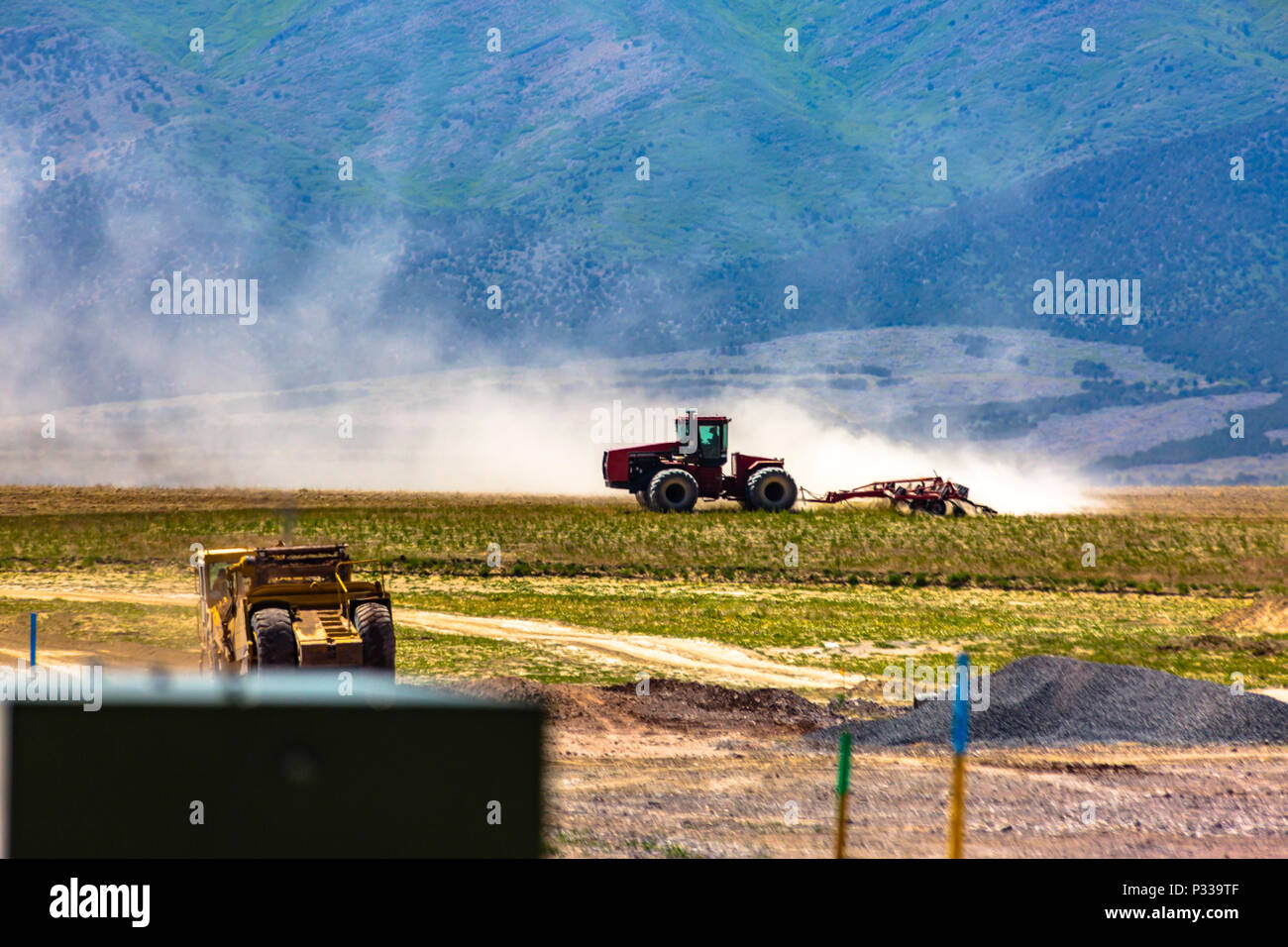 Eine große Staubwolke Fortschritte von einem Traktor schwer am Arbeiten vor Utah Berge. Stockfoto