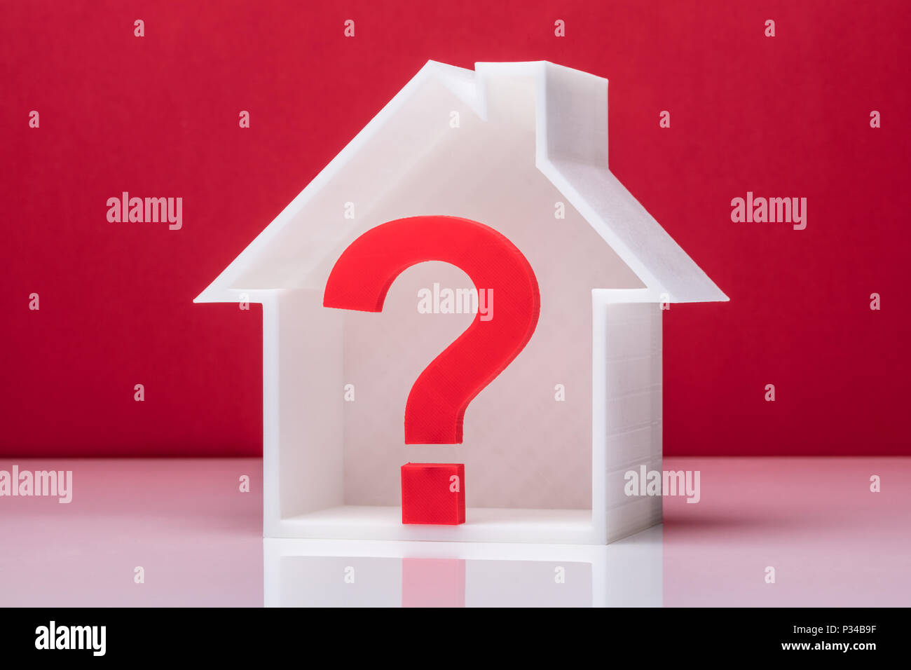 Fragezeichen im Haus Modell vor rotem Hintergrund Stockfoto