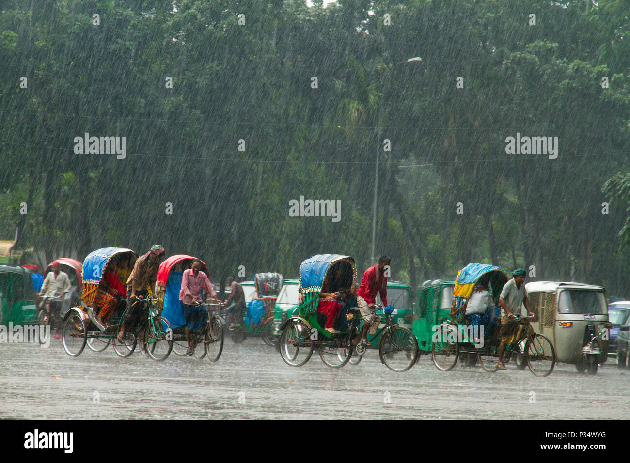 Rikschas und Fahrzeuge auf der Straße bei starkem Regen. Dhaka, Bangladesch. Stockfoto