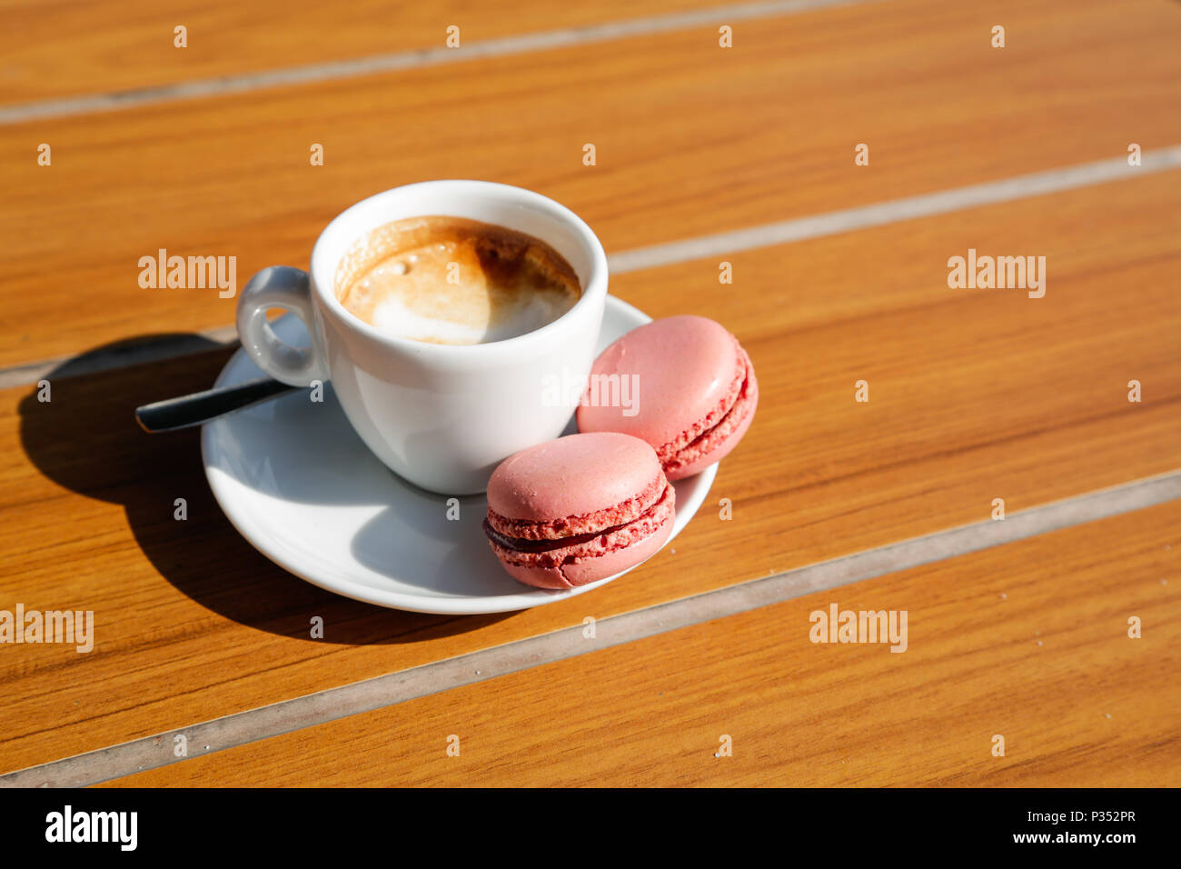 Eine Tasse Kaffee mit Erdbeerpinken Makronen, natürliches Licht auf Holztisch Stockfoto