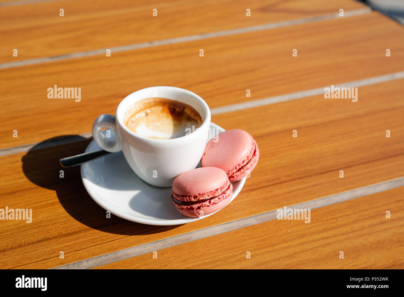 Eine Tasse Kaffee mit Erdbeerpinken Makronen, natürliches Licht auf Holztisch Stockfoto