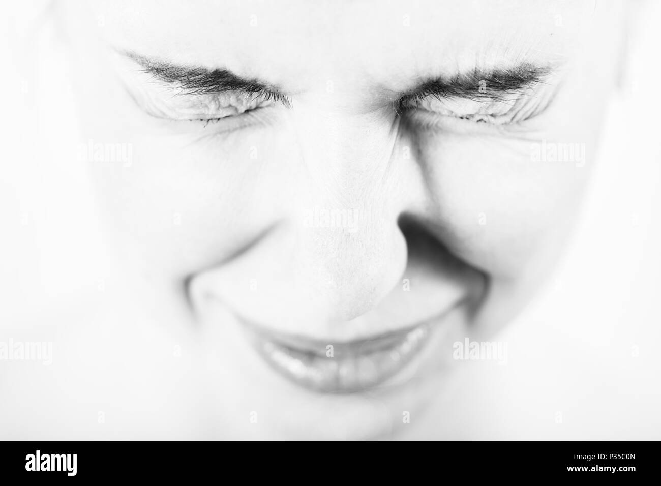 Junge Frau mit zusammengekniffenen Augen auf weißem Hintergrund, Monochrom Stockfoto