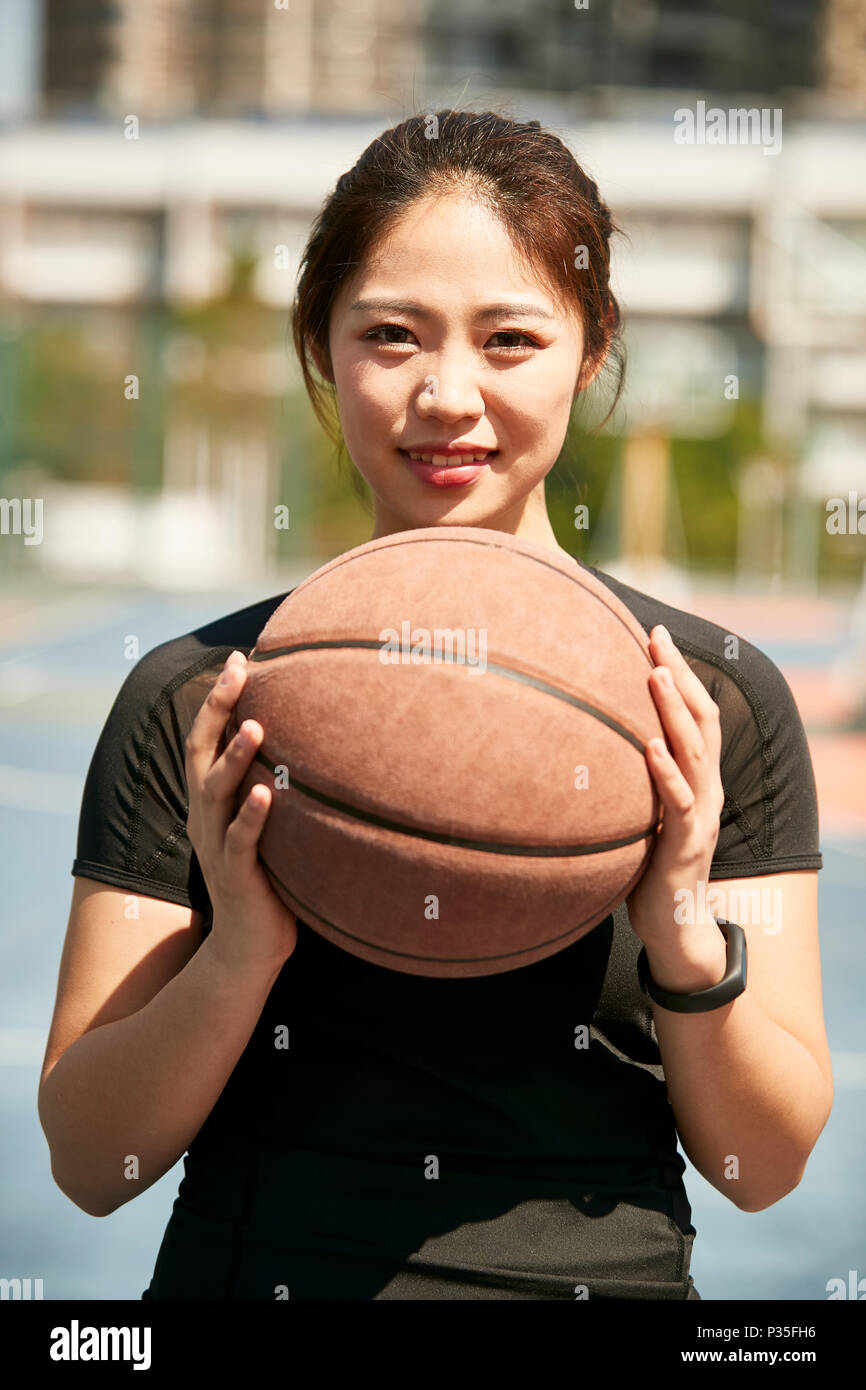 Junge asiatische Frau mit einem Basketball an der Kamera schaut lächelnd. Stockfoto